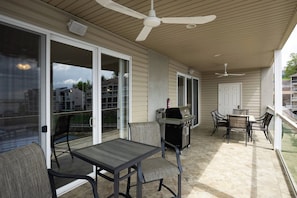 Une terrasse couverte avec une table et des chaises, un barbecue et un ventilateur de plafond.