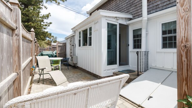 Un espace patio comprenant une chaise en osier blanc, une table et un coin salon extérieur abrité.
