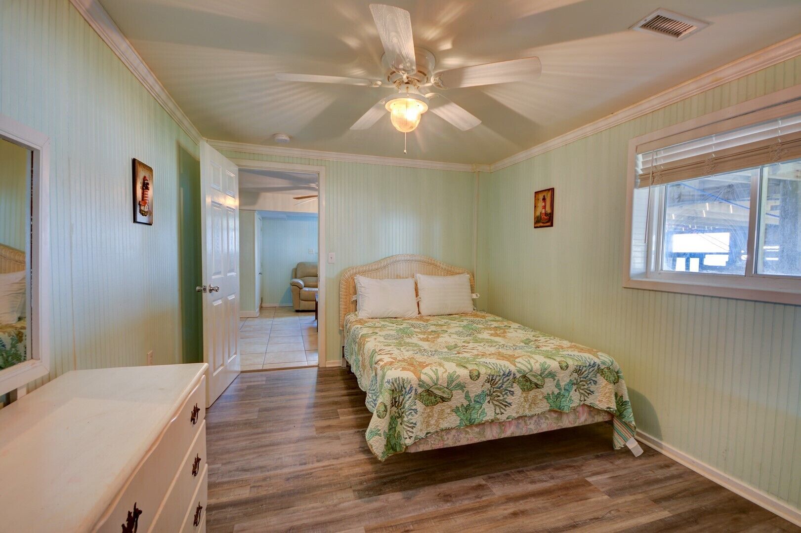 Un dormitorio con cama, ventilador de techo, ventana y puerta que da a otra habitación.