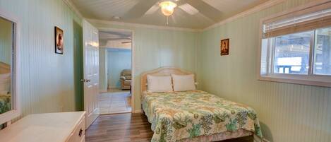 Un dormitorio con cama, ventilador de techo, ventana y puerta que da a otra habitación.