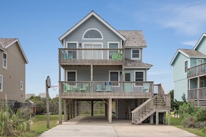 A two-story residential building with a balcony on the upper floor, a visible garage door, and a staircase leading to the entrance. - Dolphin Watch: Oceanside, Village at Nags Head (Nags Head)