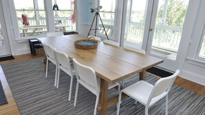 Un coin repas avec une table en bois et des chaises blanches, un panier en osier et un télescope monté sur un trépied.