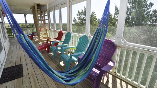 Une véranda abritée avec un hamac, des fauteuils Adirondack aux couleurs vives et une échelle en bois.