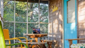 A wooden porch with a blue door, a laptop on a table, and wicker chairs. - Lindley:  Near restaurants, spacious screened porch, rooftop deck. (Ocracoke)