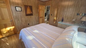 A wooden-paneled room with a bed, a dresser, and a framed picture on the wall. - Lindley:  Near restaurants, spacious screened porch, rooftop deck. (Ocracoke)