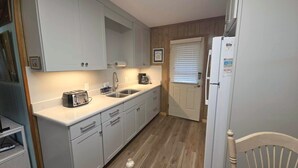A compact kitchen with white cabinets, a built-in sink, a toaster, and a refrigerator. - Lindley:  Near restaurants, spacious screened porch, rooftop deck. (Ocracoke)