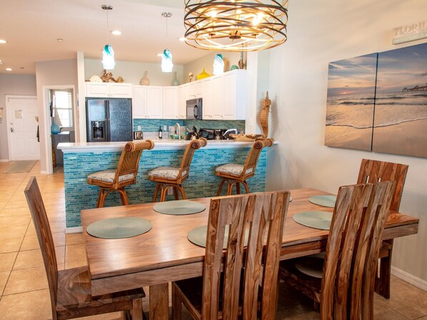 A modern kitchen with a blue backsplash, wooden chairs, and a dining table.