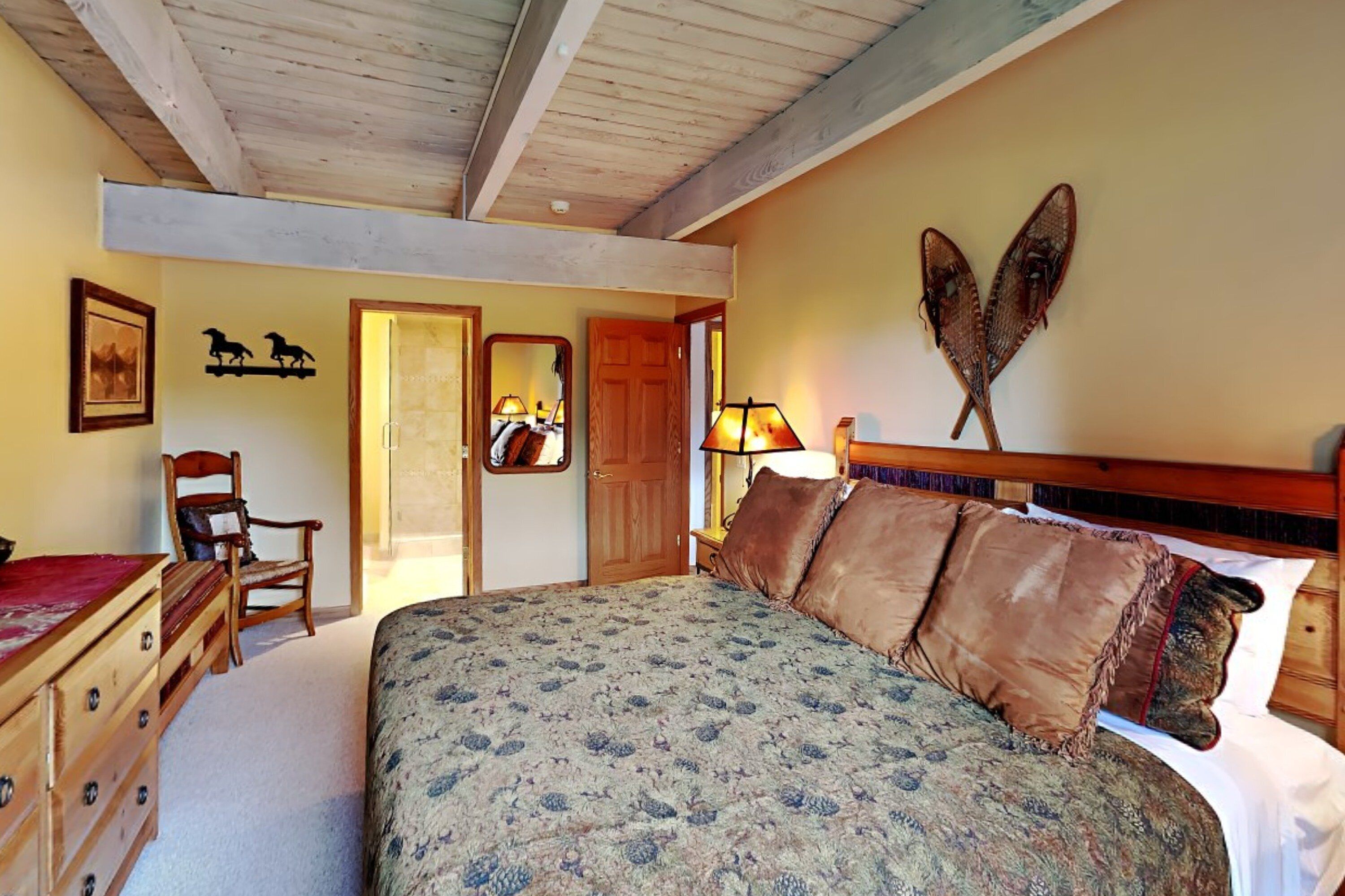 A bedroom with a large bed, wooden headboard, and a mirror above the door.