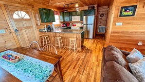 A cozy cabin-style kitchen with wooden floors, a dining area with a table and chairs, and a kitchenette with a refrigerator and microwave. - Absolute High | 3BR Cabin w/ Long-Range Mountain Views, Game Room & Deck (West Jefferson)