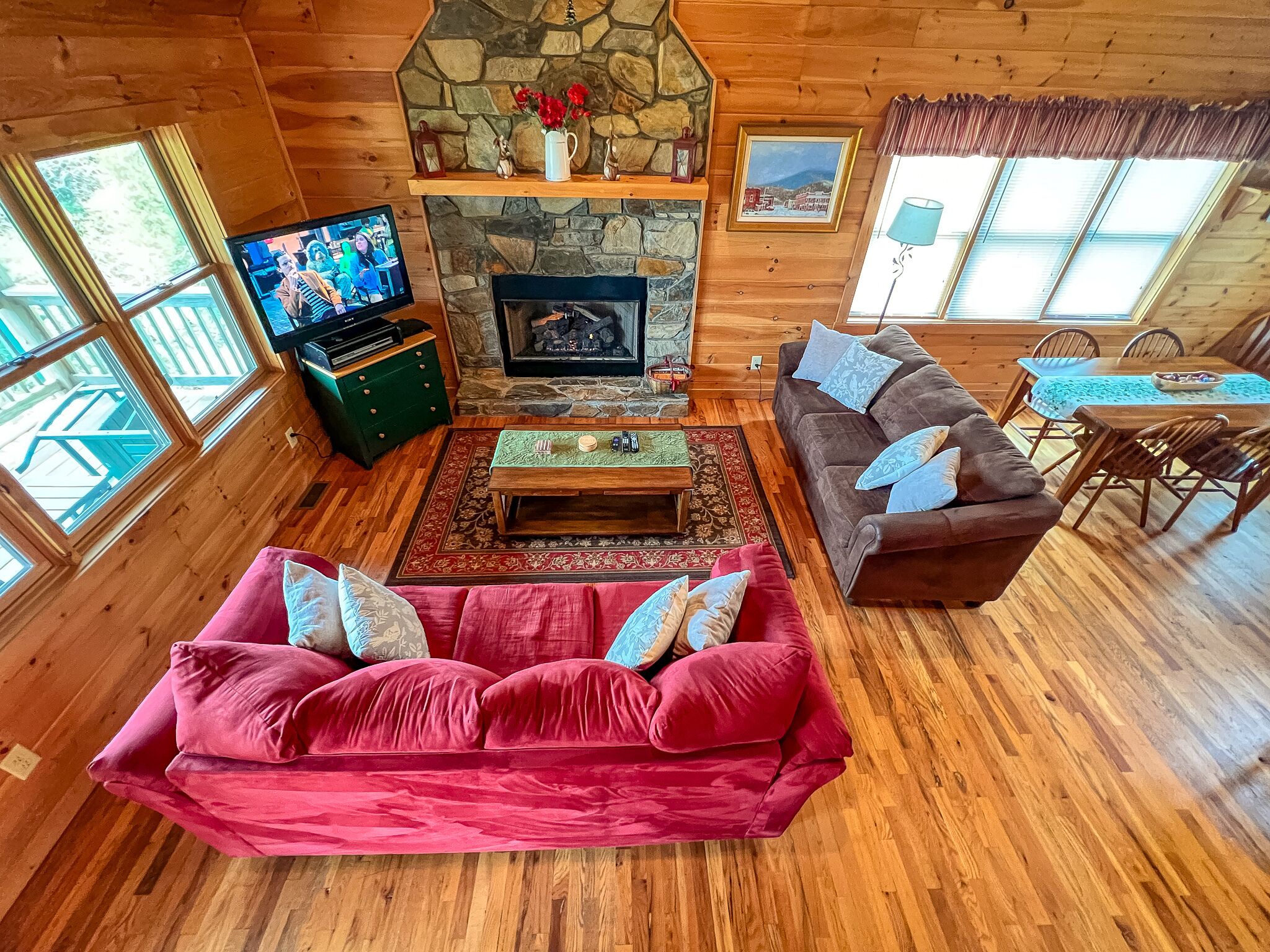 A cozy cabin interior with a stone fireplace, wooden walls, a red sofa, and a dining area.