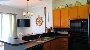 Una cocina moderna con armarios de madera, un microondas negro y un adorno con forma de timón.