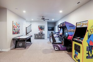 Una habitación con mesa de billar, juegos de arcade y ventilador de techo.