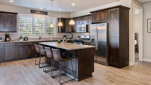 A modern kitchen with dark wood cabinets, a large island with bar stools, stainless steel appliances, and pendant lighting. - Awesome Arcade House: Private Hot Tub, Game Room, Theater! (Santa Clara)
