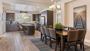 A modern kitchen with dark wood cabinets, a central island, and a dining area with a chandelier. - Awesome Arcade House: Private Hot Tub, Game Room, Theater! (Santa Clara)