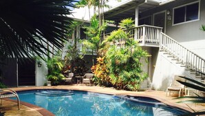 Una piscina rodeada de plantas y mobiliario de exterior, con una escalera que lleva a un nivel superior.