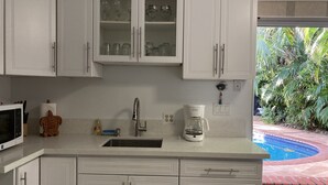 Una cocina con armarios blancos, un fregadero, una cafetera y vista a una piscina.