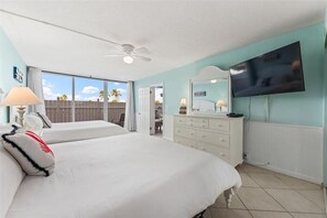 Two large beds with white linens and pillows, a dresser, and flat-screen TV in a stylish room with a view of palm trees.