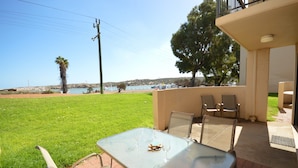 An outdoor patio with a table and chairs, overlooking a grassy area and a body of water. - Riverview Holiday Waterfront Apt  11 - 2 Storey - Kalbarri, WA (Kalbarri)