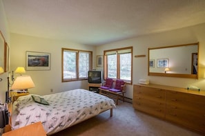 Une chambre à coucher comprenant un lit, une télévision, une chaise, une commode et un miroir.