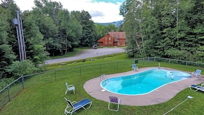 A swimming pool with a surrounding fence, grass, and a few lounge chairs. - Three bedroom townhouse, conveniently located (Killington)