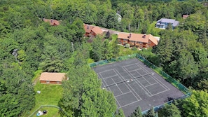 Vue aérienne d’un quartier résidentiel avec un court de tennis entouré d’arbres et de maisons.