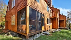 A wooden cabin with large windows, a deck, and a stone foundation. - Three bedroom townhouse, conveniently located (Killington)