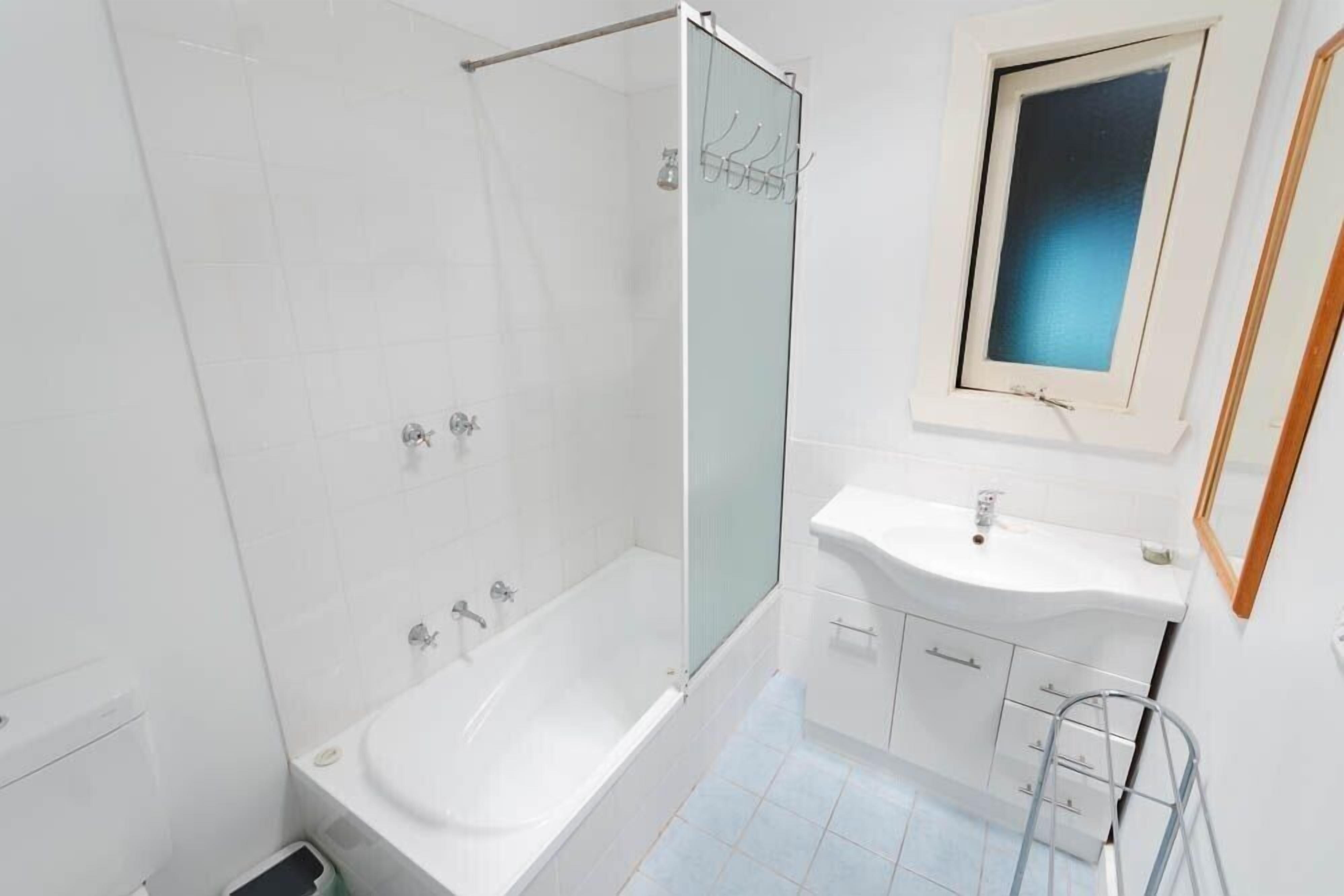 A modern bathroom with a glass-enclosed shower, a white sink, and a small window.