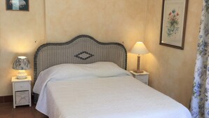 A neatly made bed in a room with a tiled floor, two bedside tables with lamps, and a floral curtain.