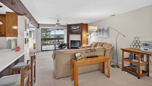 A living room with a sofa, a wooden coffee table, a fireplace, a TV, and a balcony with outdoor furniture. - Knolls 1122 - Two Bedroom Apartment, Sleeps 6 (Osage Beach,)