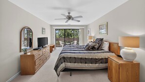 A bedroom with a bed, a TV, a ceiling fan, a dresser, a lamp, and a view of the outdoors. - Knolls 1122 - Two Bedroom Apartment, Sleeps 6 (Osage Beach,)