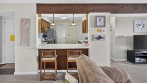 A compact living space with a kitchenette, two bar stools, a sofa, and a television. - Knolls 1122 - Two Bedroom Apartment, Sleeps 6 (Osage Beach,)