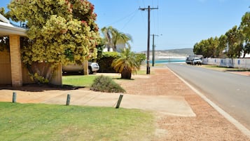 A residential street with a house, a driveway, a tree, and a view of the ocean.