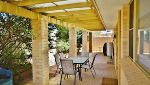 Un patio cubierto con una mesa y sillas, pilares de ladrillo y vistas al exterior.