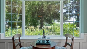 Une baie vitrée donnant sur un jardin, une table avec un jeu de société et deux chaises.