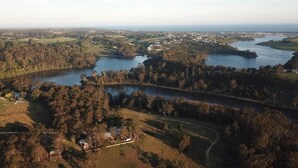 An aerial view of a coastal area with a river, surrounding greenery, and a small settlement.