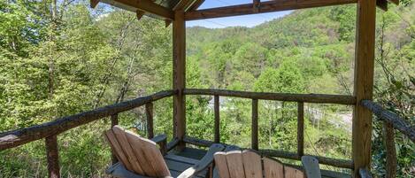 Een houten terras met Adirondack-stoelen met uitzicht op een beboste helling.