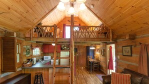 A rustic cabin interior with a loft bedroom, a kitchen area, and a living room with a leather sofa. - Log Cabin with Private Outdoor Hot Tub (Hot Springs)