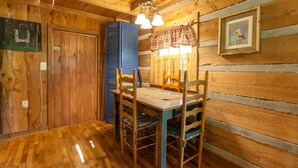 A wooden cabin interior with a dining table, chairs, a blue cabinet, and a framed picture on the wall. - Log Cabin with Private Outdoor Hot Tub (Hot Springs)