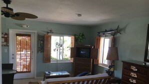 Une chambre avec un lit, un bureau, une commode, un téléviseur et une fenêtre avec des stores.