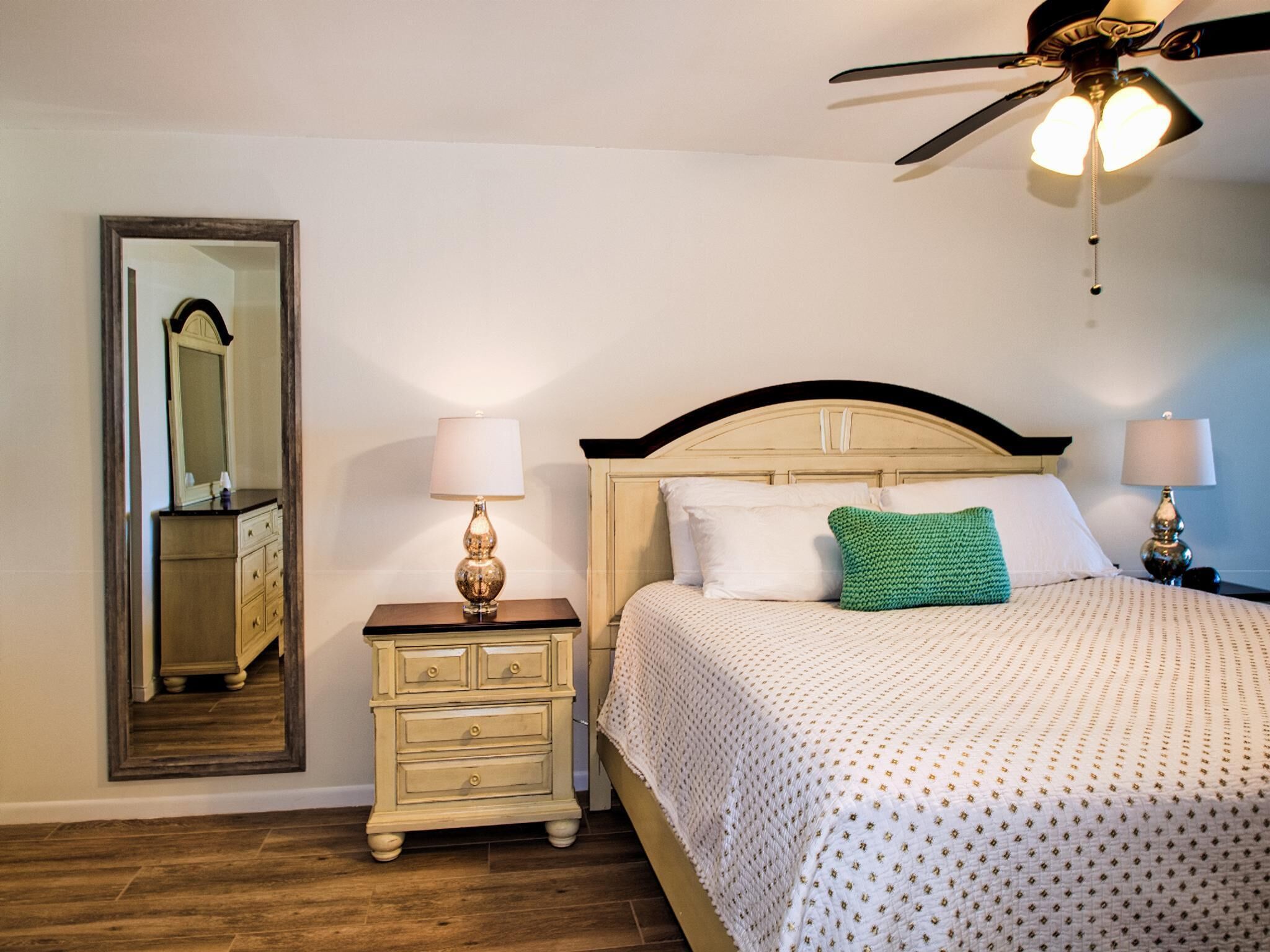 A bedroom with a bed, nightstands, a mirror, and a ceiling fan.