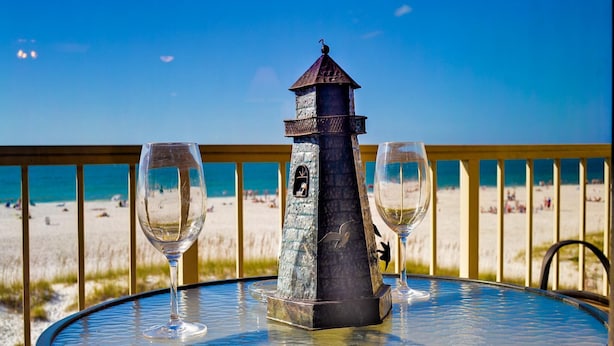 Una mesa redonda con un centro decorativo de faro, dos copas de vino vacías y una vista a la playa al fondo.