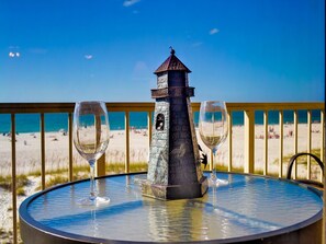 Ein runder Tisch mit einer dekorativen Leuchtturm-Mittelstück, zwei leeren Weingläsern und Blick auf den Strand im Hintergrund.