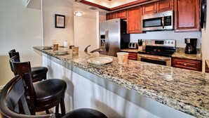 Una cocina con encimeras de granito, electrodomésticos de acero inoxidable, armarios de madera y una zona de bar con taburetes.