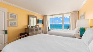 Ett hotellrum med två sängar, en byrå, en tv och en balkong med utsikt över havet.