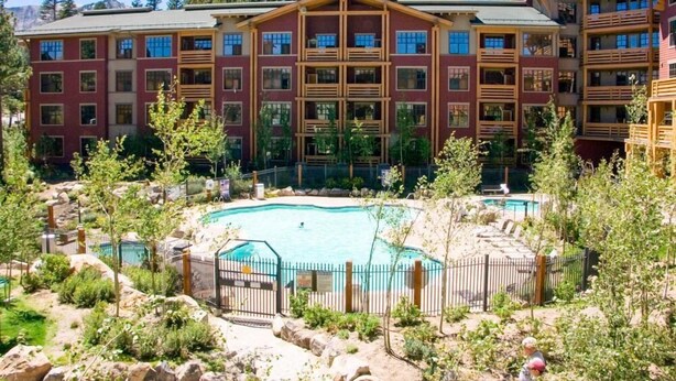A multi-story hotel with a pool area surrounded by trees and rocks.