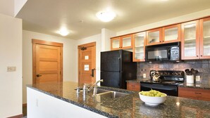 A kitchen with granite countertops, a black refrigerator, a microwave, and wooden cabinets.