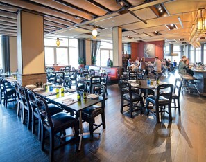 A spacious restaurant with multiple dining tables and chairs, large windows, and a modern ceiling design.