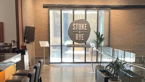 A restaurant interior with a sign reading 'STOKE & RYE' by Chef Richard Sandoval, a glass railing, and a potted plant.