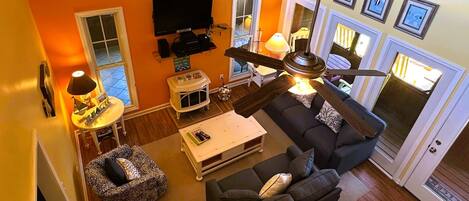 Een woonkamer met een donkere bank, een salontafel, een televisie en een plafondventilator.