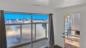A room with a large sliding glass door leading to a balcony with a view of boats and the sea.